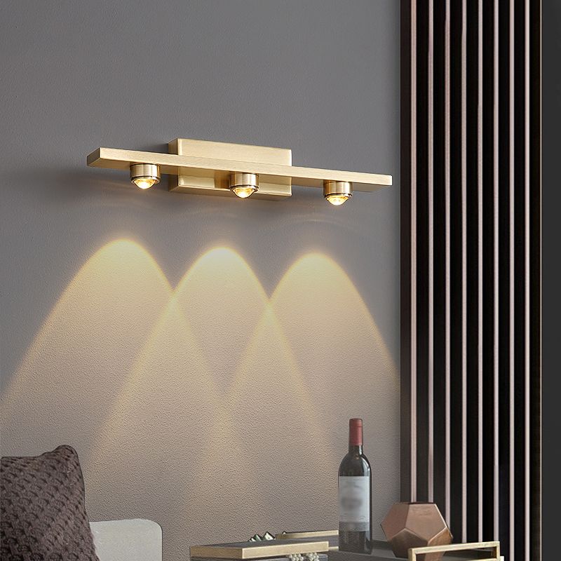 Angled Leigh three-light gold-tone lamp above a side table beside upholstered furniture and a slatted panel