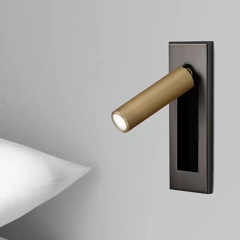 Gold Orr cylindrical spotlight head tilted from a dark wall plate beside a shelf