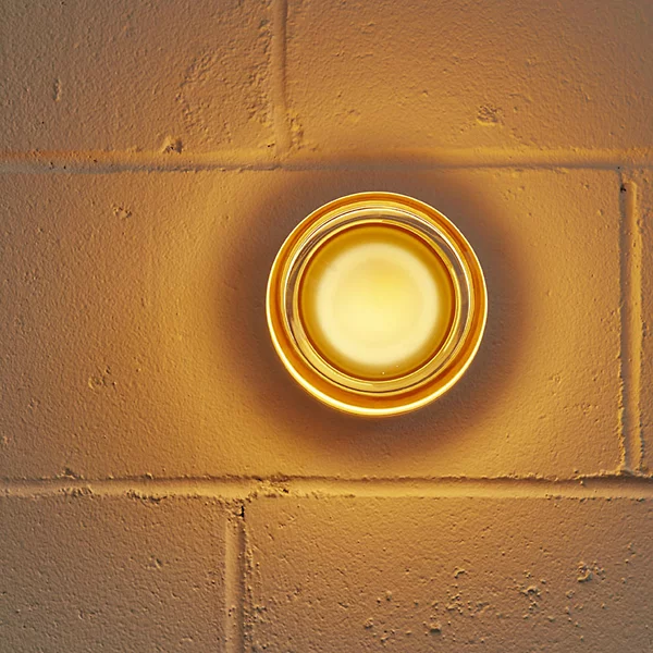Front view of a glowing amber round wall light with concentric curved edges on a brick wall