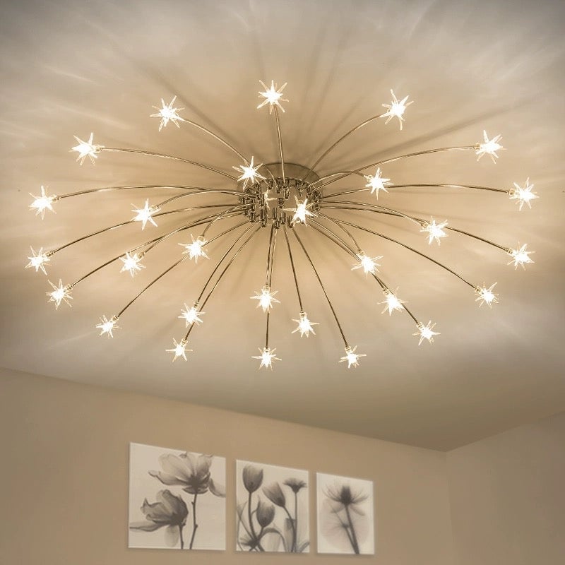Upward view of chrome-tone lit star ceiling fixture above three floral wall prints, with radiating ceiling shadows