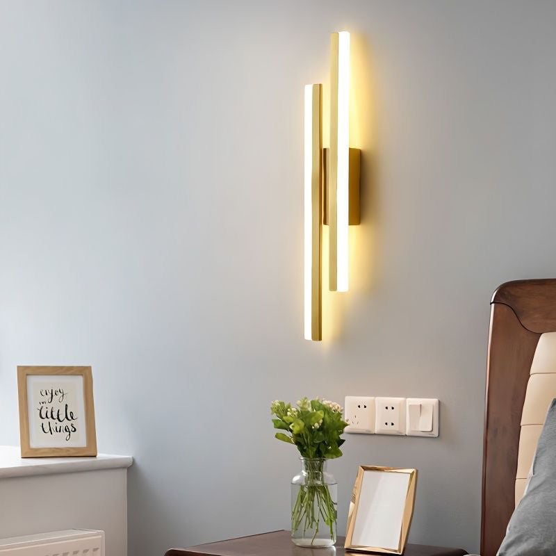 Gold Right-layout bar wall light beside a bedhead, flowers and a framed picture