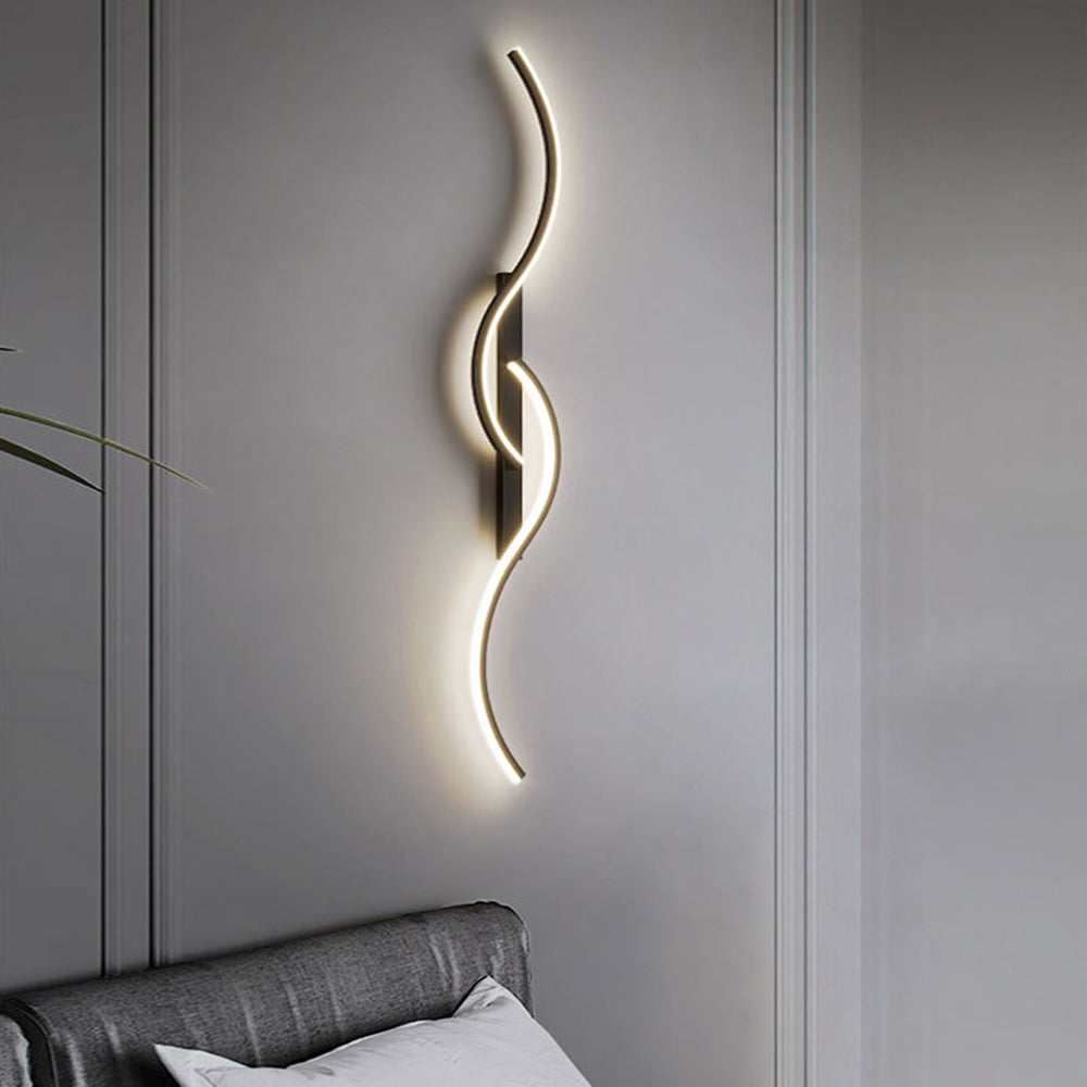 Black wave wall light glowing vertically above a gray upholstered headboard on a paneled wall