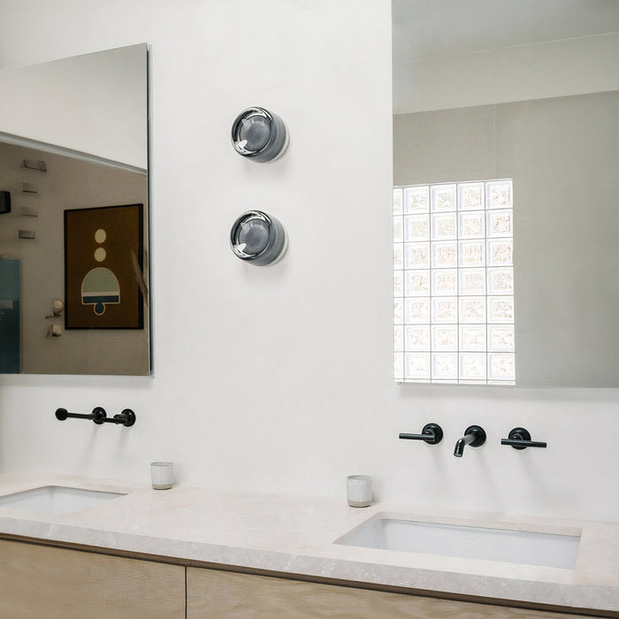 Two unlit smoke-grey round wall lights between mirrors above a double basin and black taps