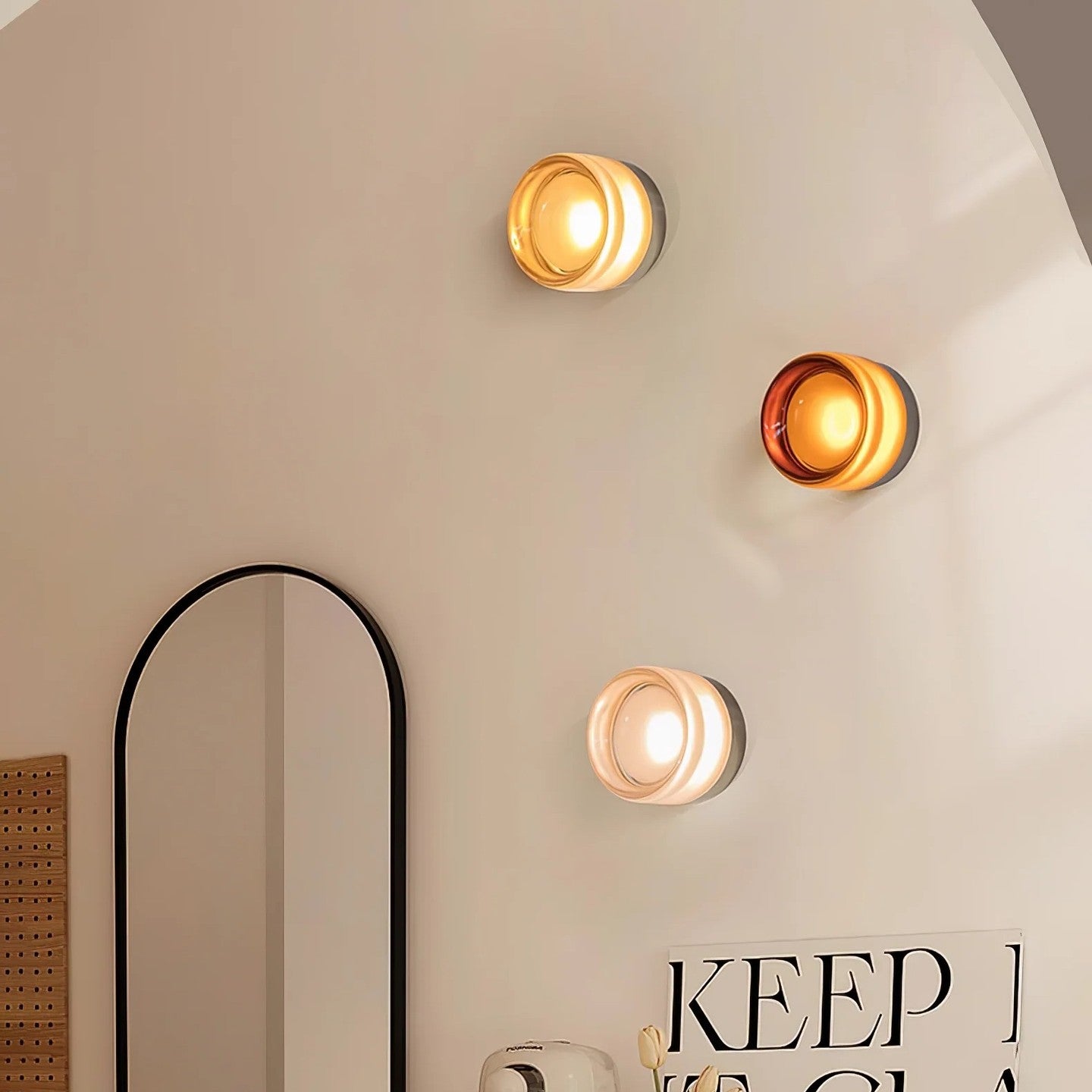 Three glowing round wall lights with pale and amber rims beside an arched mirror