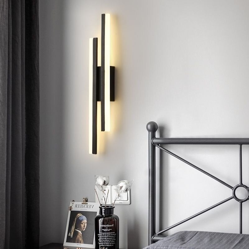 Black Right-layout offset-bar wall light beside a metal bedframe, books and a vase