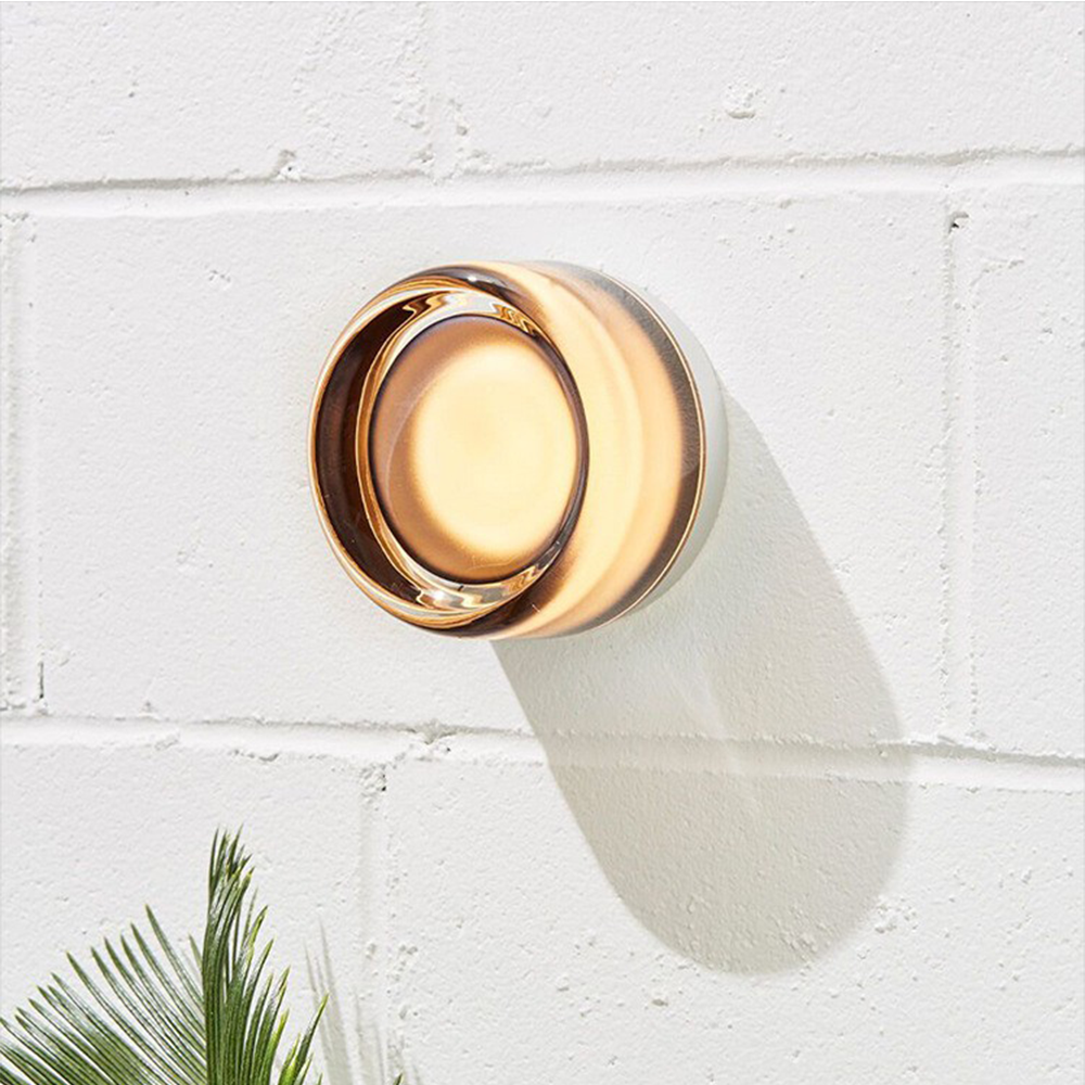 Smoke-tinted round wall light glowing on white brick above a palm leaf with a long cast shadow