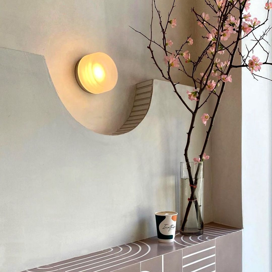 Pale round wall light above a tiled ledge with a cup and clear vase of pink flowering branches