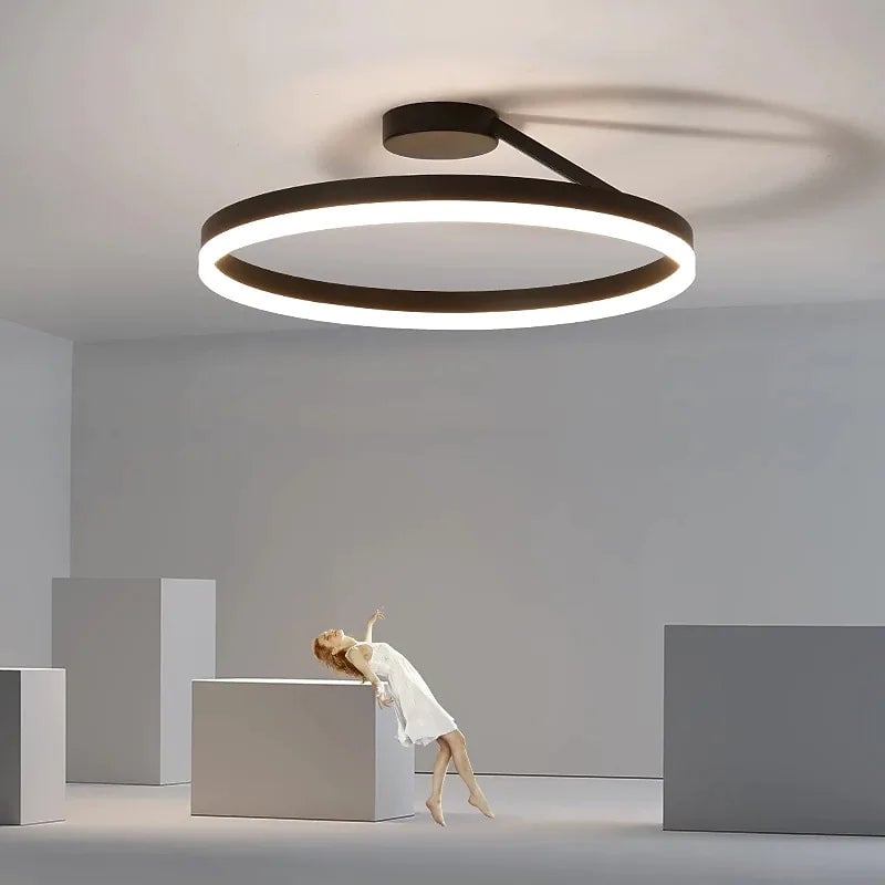 Black illuminated ring ceiling fixture above gray geometric blocks and a woman figure