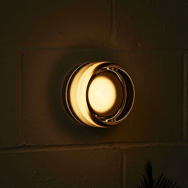 Smoke-tinted round wall light glowing warmly on brick in a dark room