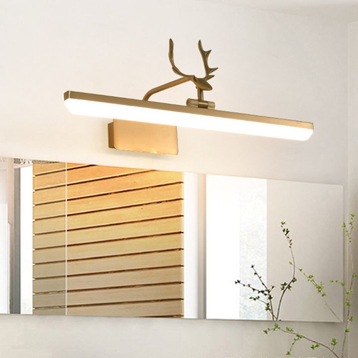 Gold-tone antler wall light above a horizontal mirror reflecting wooden slats, with a leafy branch at the right