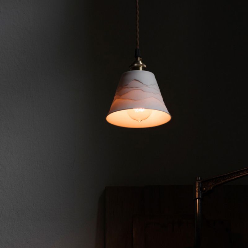 View from below of lit Lottie ceramic cone with visible bulb below the opening against a dark wall