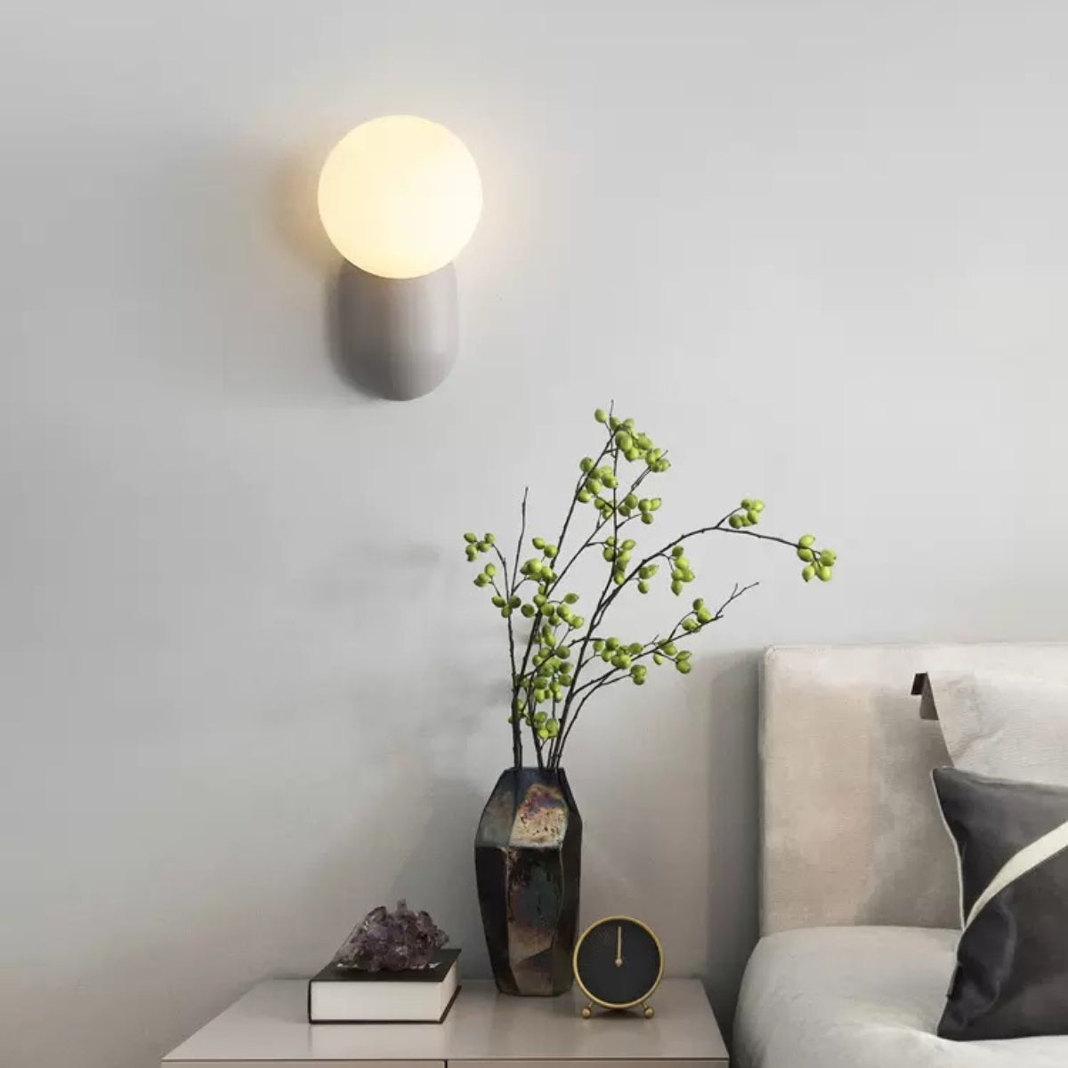 Grey Hailie glass globe wall lamp beside a bed and side table