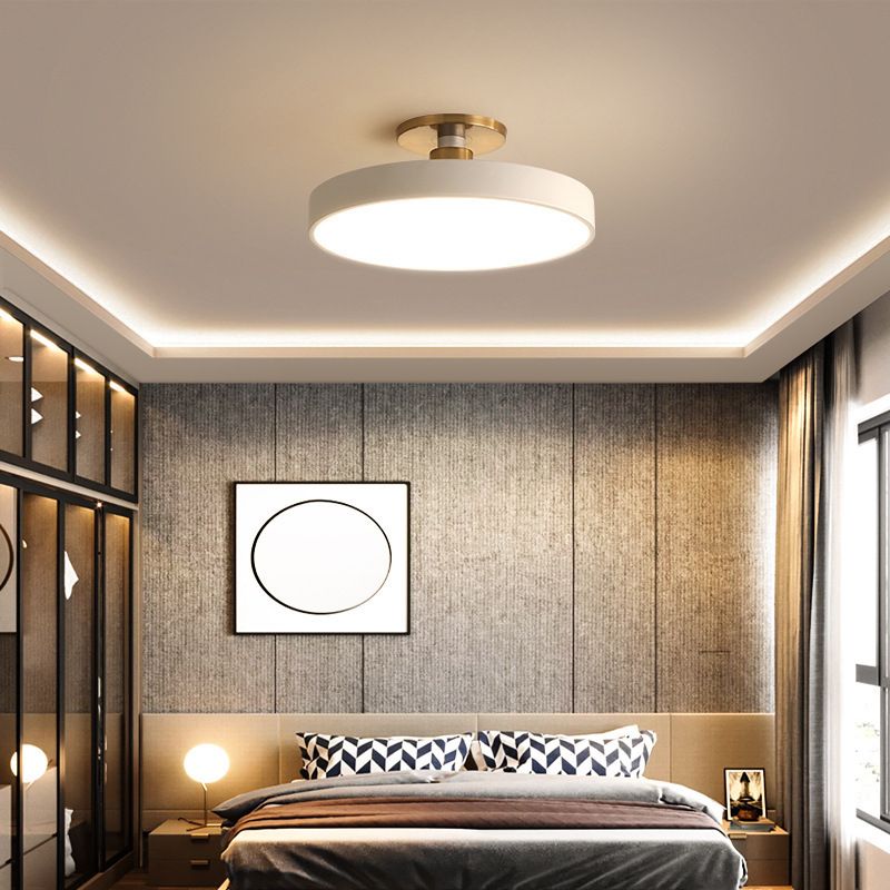 White round ceiling fixture illuminated above a bedroom with geometric pillows and circular framed art