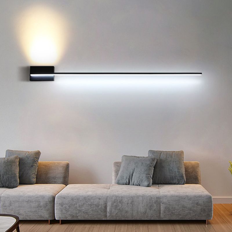 Black linear wall light above a grey sofa with cool-looking lower light and a warm upward patch