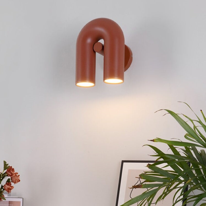 Red option photo, angled U-shaped wall light with two luminous ends above framed art, pink flowers and long green leaves
