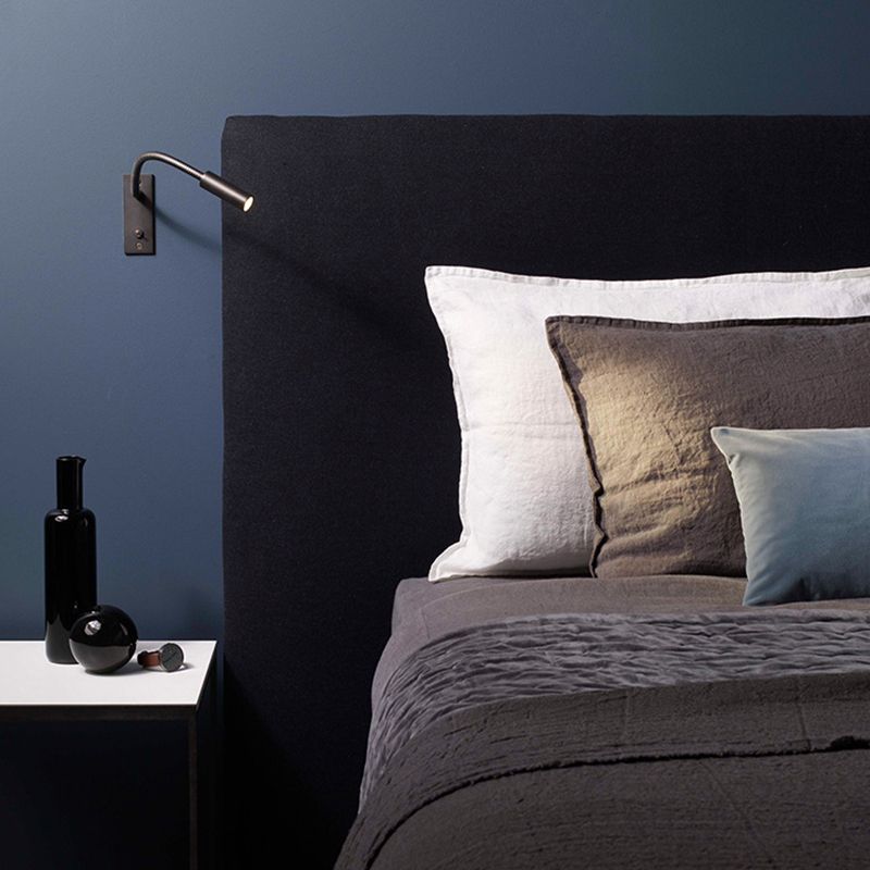 Orr gooseneck reading lamp mounted on a dark blue wall beside a bed.