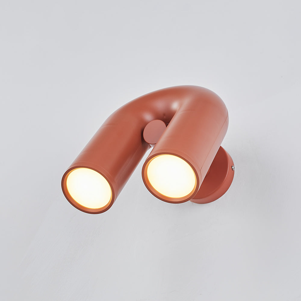 Red U-shaped fixture tilted forward on pale wall, two lit circular diffusers, central joint and round backplate