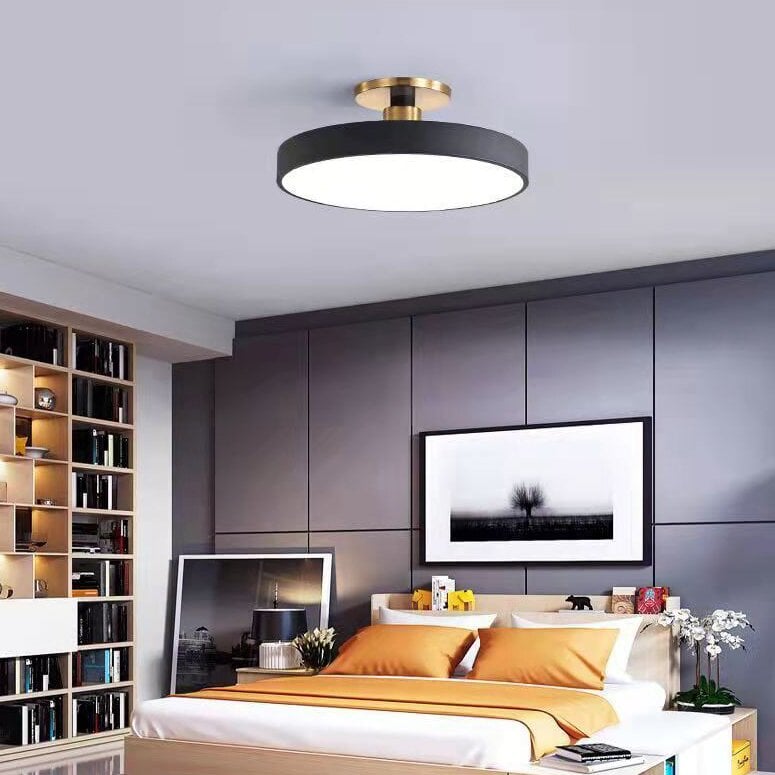 Black round ceiling fixture above a bedroom with yellow pillows, gray wall panels and a bookcase