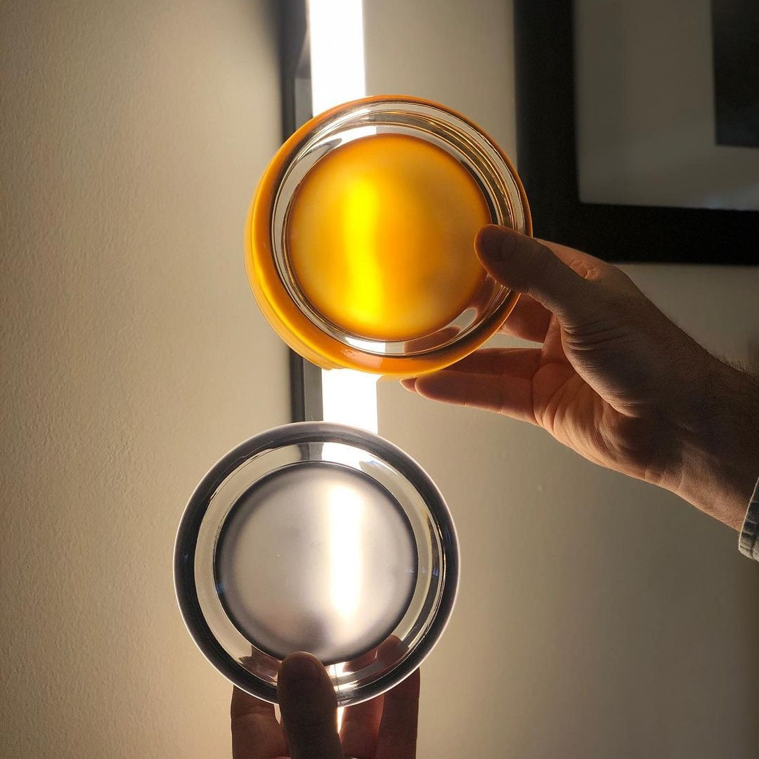 Hands holding amber and smoke-grey circular shades in front of a window
