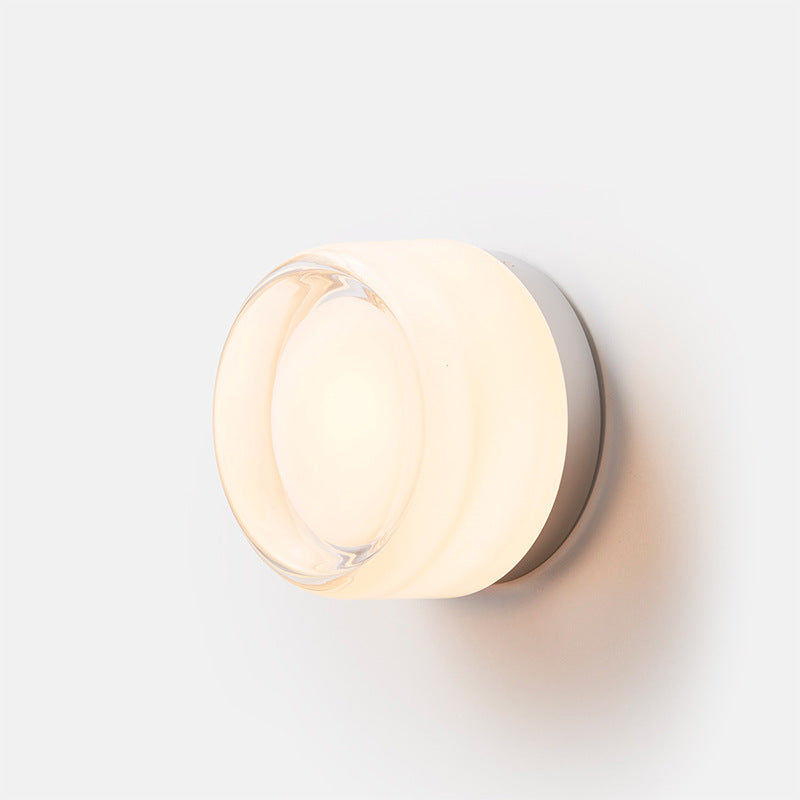 Isolated lit white round wall light with a curved rim, recessed centre and silver-coloured circular backplate