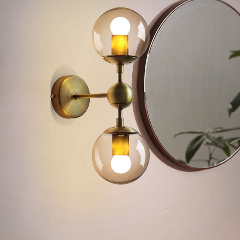 Gold Valentina two-globe wall light beside a round mirror, with visible lit bulbs