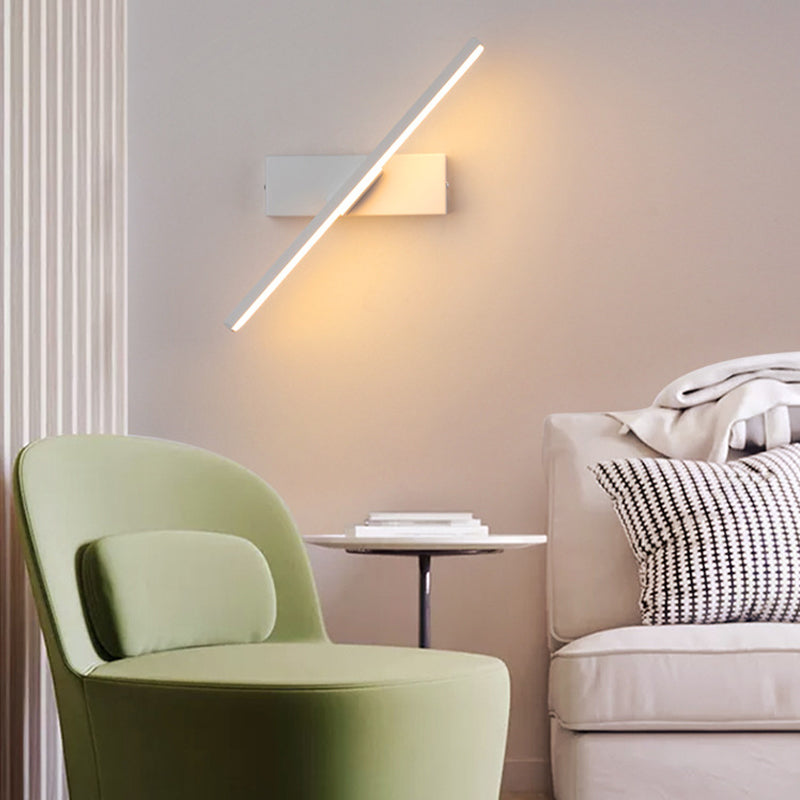 White bar wall light tilted diagonally above a green armchair