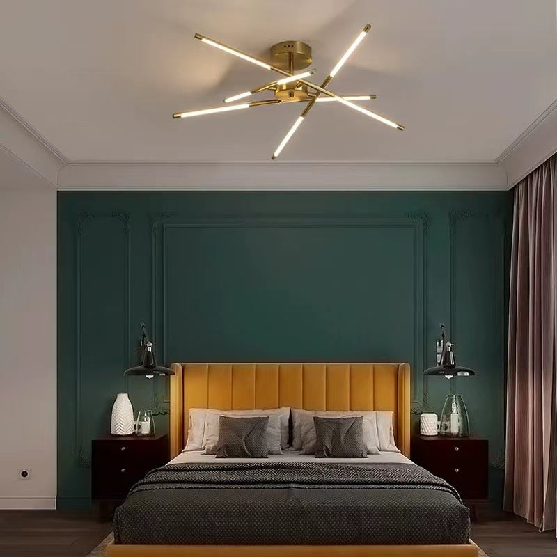 Gold crossed-bar ceiling light above a bed with a mustard headboard and green wall panels