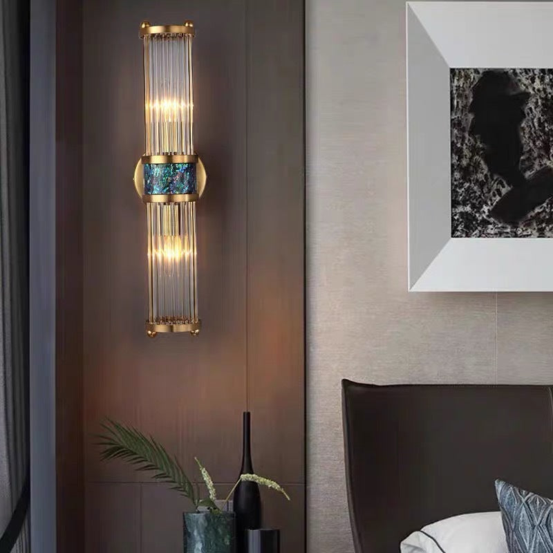 Tall gold-tone rod wall light beside a bed, headboard, plants and framed artwork