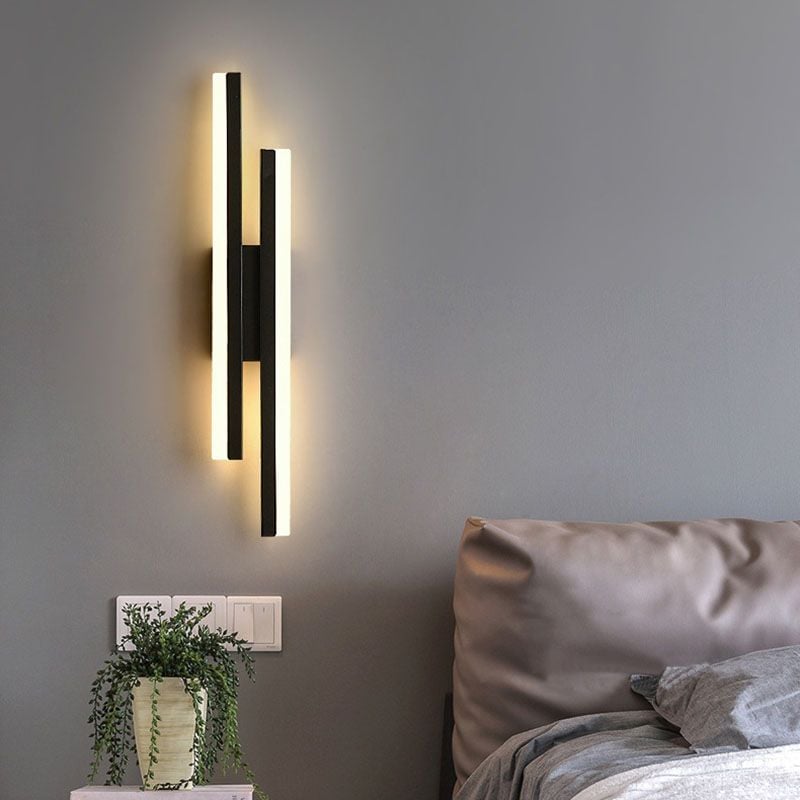 Black Left-layout bar wall light beside a grey bed, potted plant and wall switches