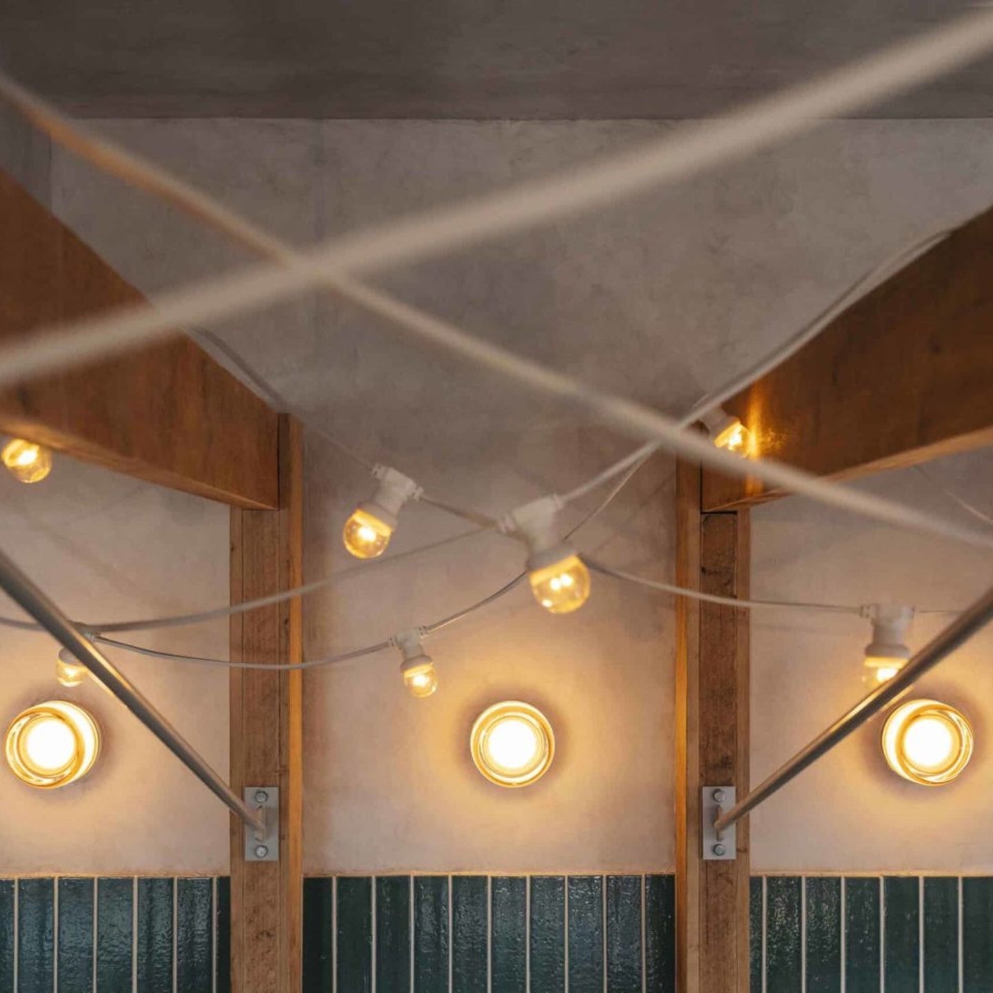 Three glowing round wall lights beneath wooden beams and string lights above a tiled wall