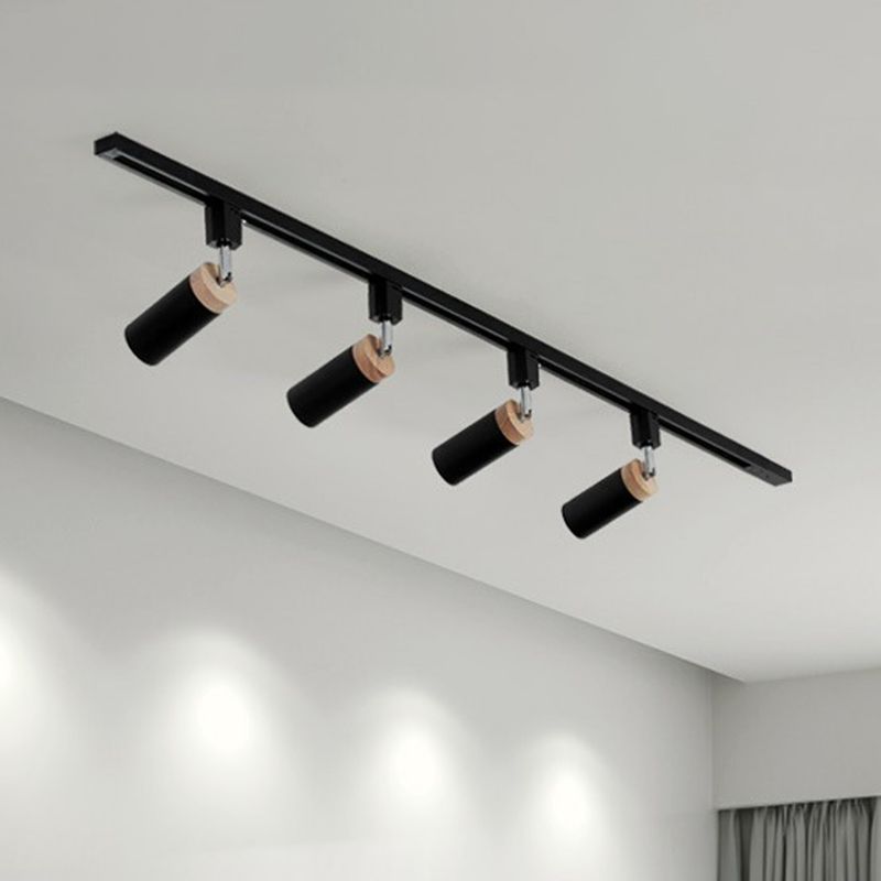 Black four-head rail light with tilted tubular spotlights casting pools of light on a wall