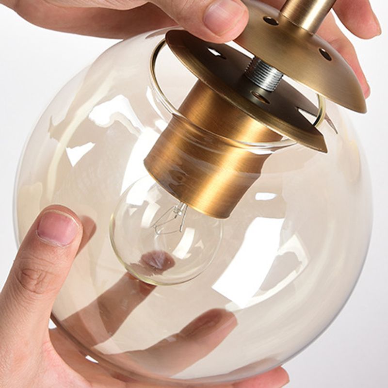 Hands positioning a clear Valentina glass globe beneath its Gold metal mounting plate