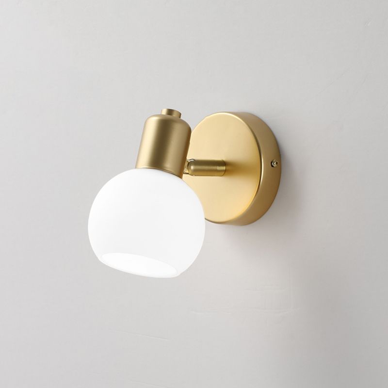 Single Gold wall light with a white open-bottom globe and short arm against a pale wall