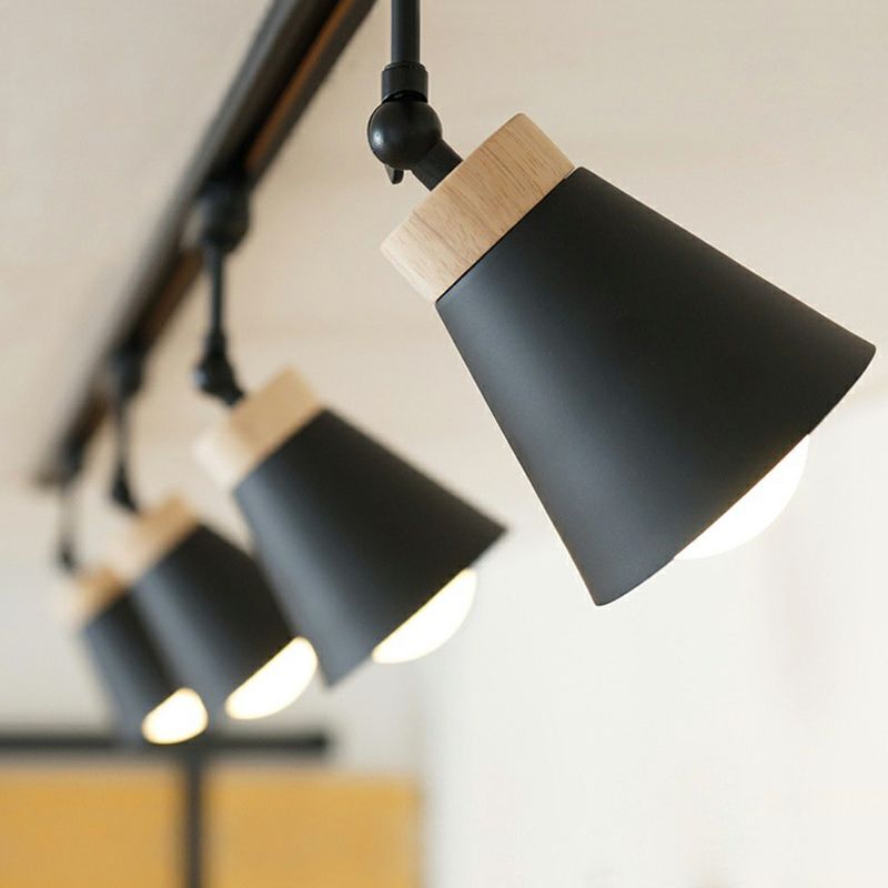 Close-up of four black Haney cone spotlights on a ceiling rail, foreground head angled at the neck, wood-tone collars and lit bulbs