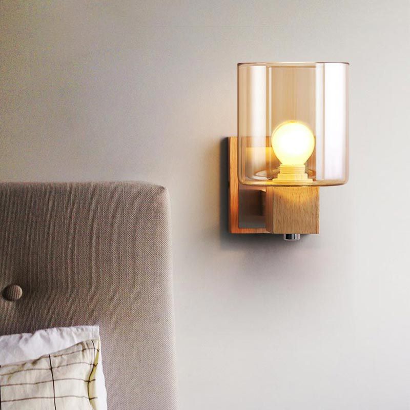 Eryn wood-and-glass wall light with the cylinder above its wooden holder beside an upholstered headboard