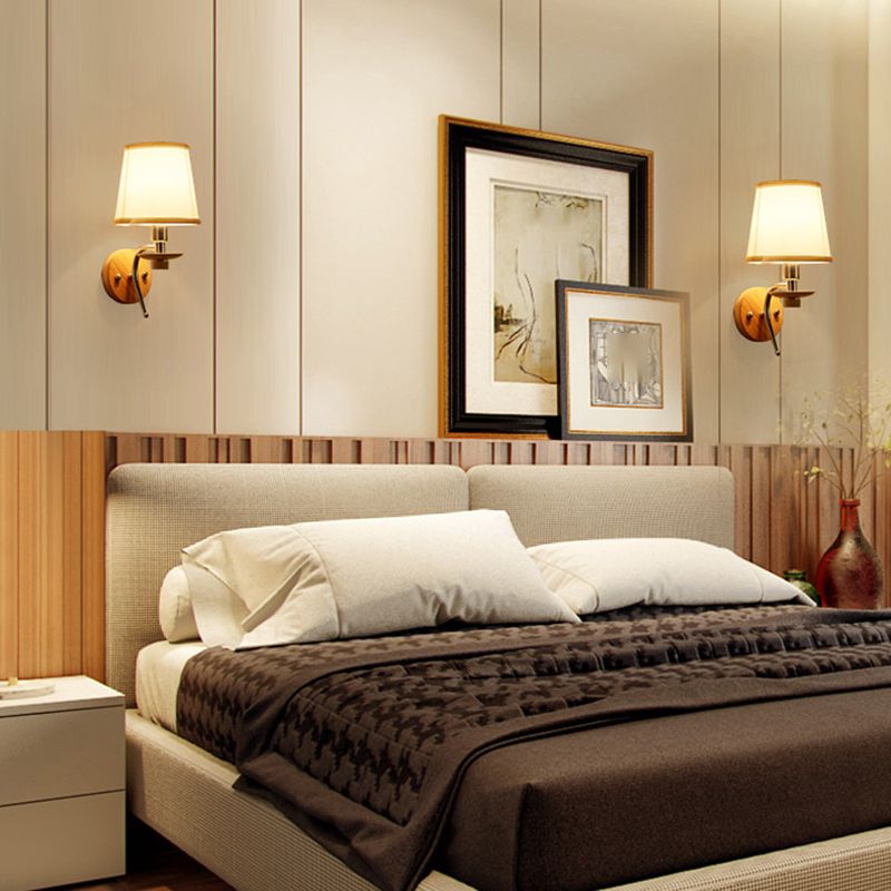 Two Eryn fabric-shade wall lights with round wood plates on either side of a bed and framed artwork