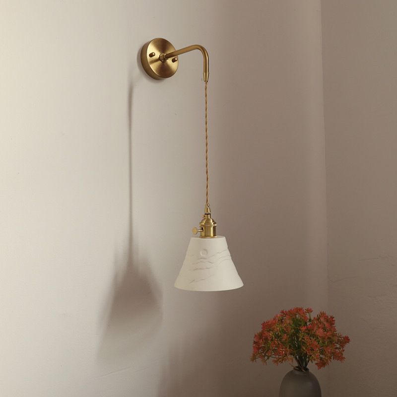 Unlit white Lottie relief cone on a twisted cord below a gold-tone round wall fitting beside flowers