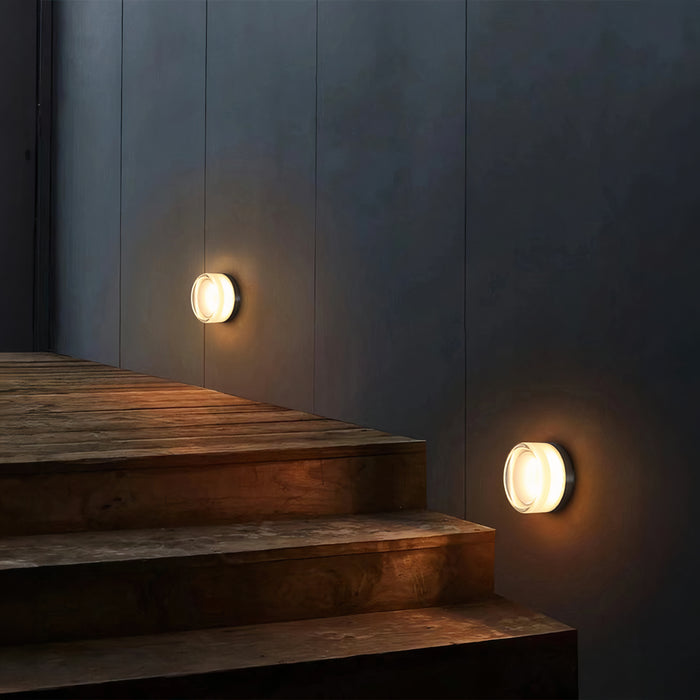 Two pale round wall lights glowing beside wooden stairs against a dark panelled wall