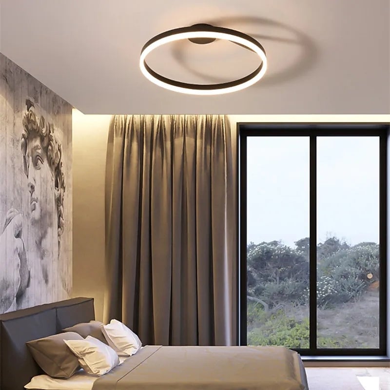 Black illuminated ring ceiling fixture above a bedroom with tall window, curtain and large portrait