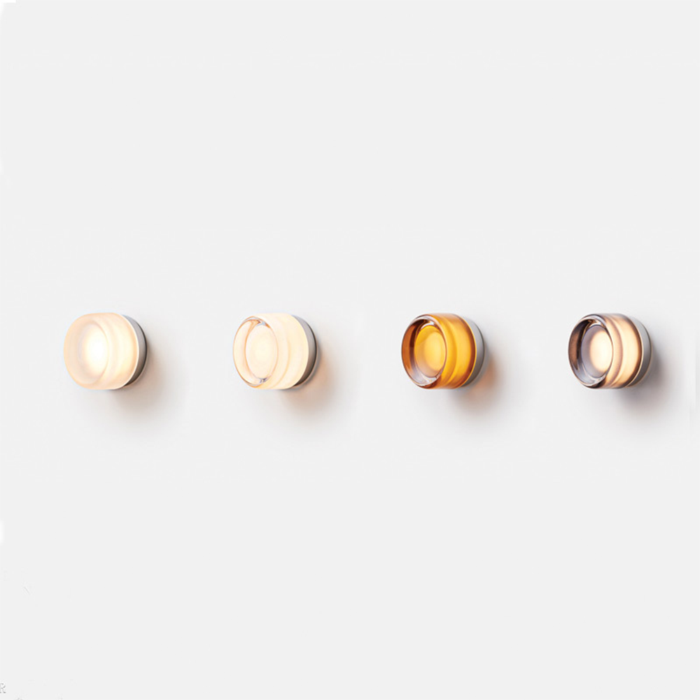Four round wall lights in a horizontal row showing pale, clear-looking, amber and smoke-tinted appearances