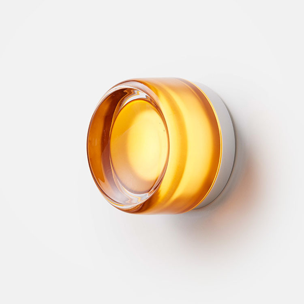 Three-quarter view of the glowing amber circular shade with a deep rounded rim and silver-coloured backplate
