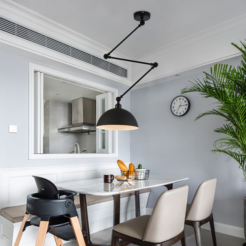 Black dome pendant on an articulated ceiling arm over a dining table near a kitchen opening and plant