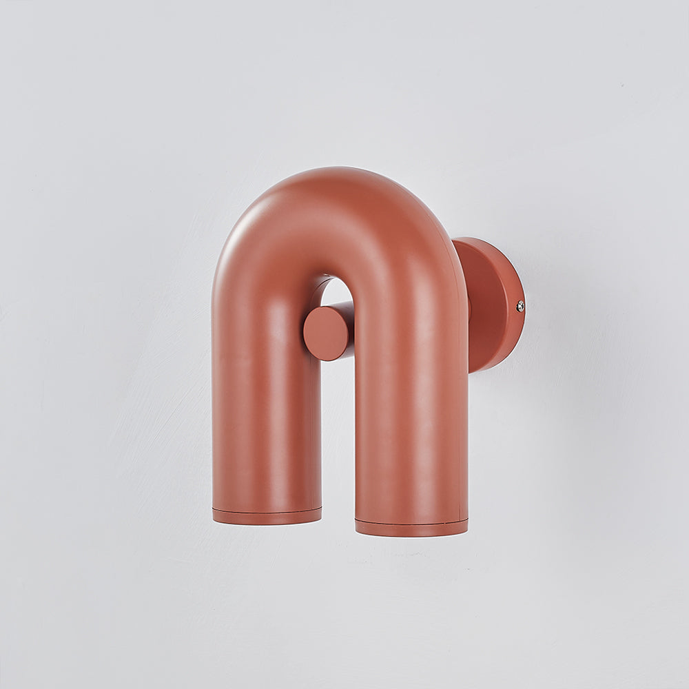 Unlit red U-shaped fixture at three-quarter angle on pale wall, round backplate, side screw and central boss visible