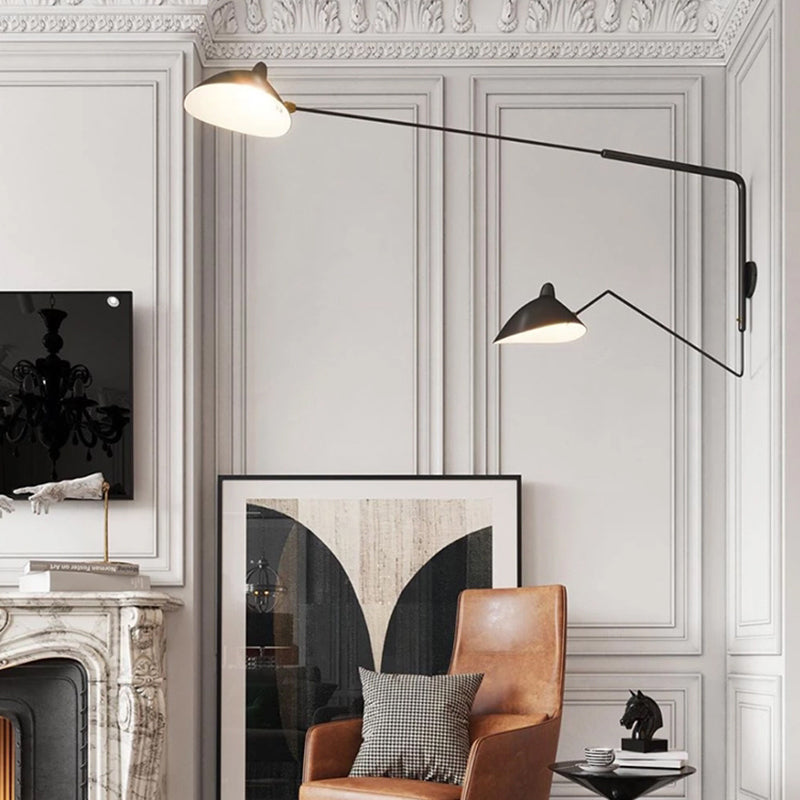 Two-head black wall light with unequal arms above a leather armchair