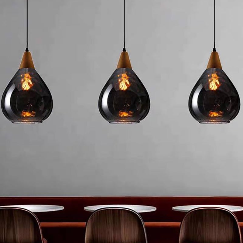 Three wide smoke-grey Avi pendants with oval glass texture above tables and rounded chairs against pale wall