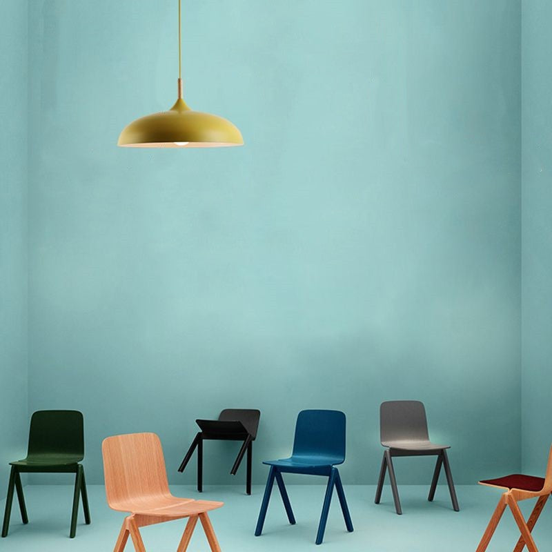 Yellow shallow dome pendant against a turquoise wall above a display of colorful chairs