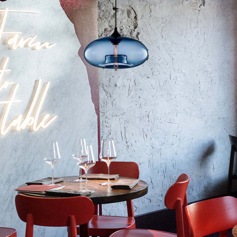 Blue oval glass pendant light above a round dining table with Red chairs, wine glasses and illuminated wall script