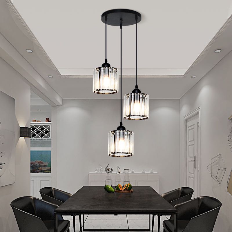 Black three-cylinder glass cluster staggered from round canopy above dark table, black chairs and white sideboard