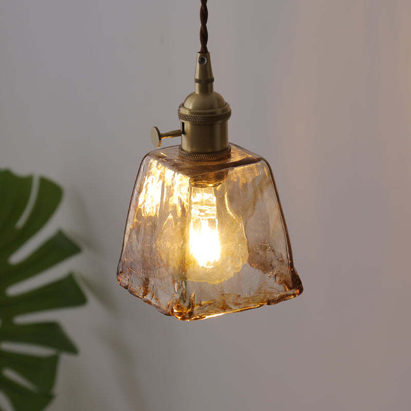 Close-up of a tapered amber glass pendant beside green foliage