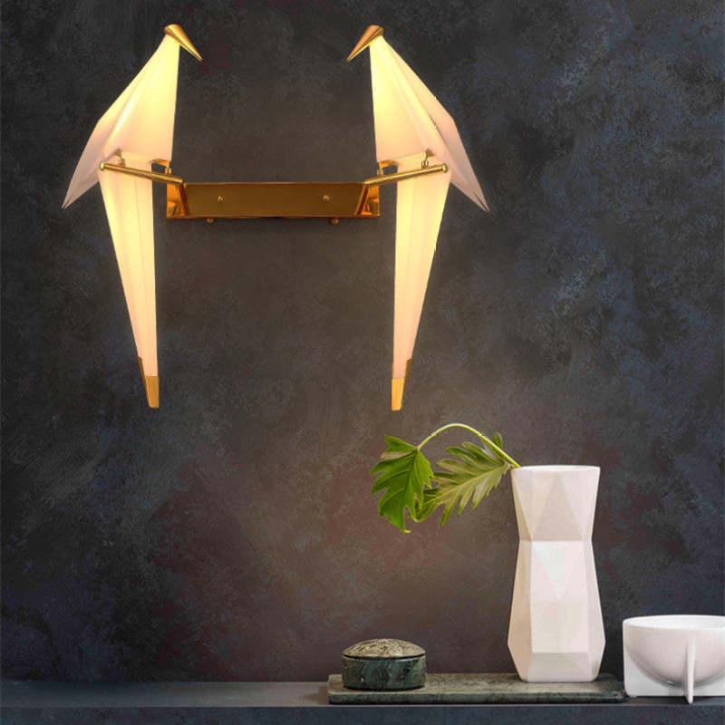 Lit two-bird Clifford wall light on a dark wall above a vase with a leaf, small box and bowl